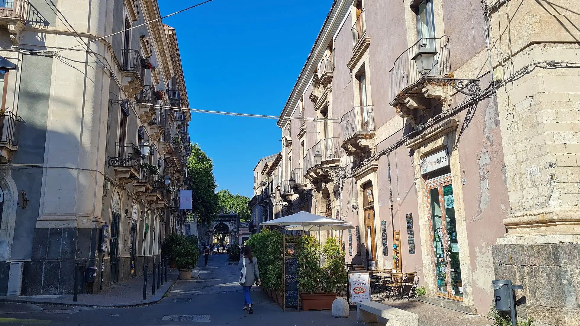 A quieter stretch of Via dei Crociferi, lined with carved stone balconies and ending at a gateway under trees
