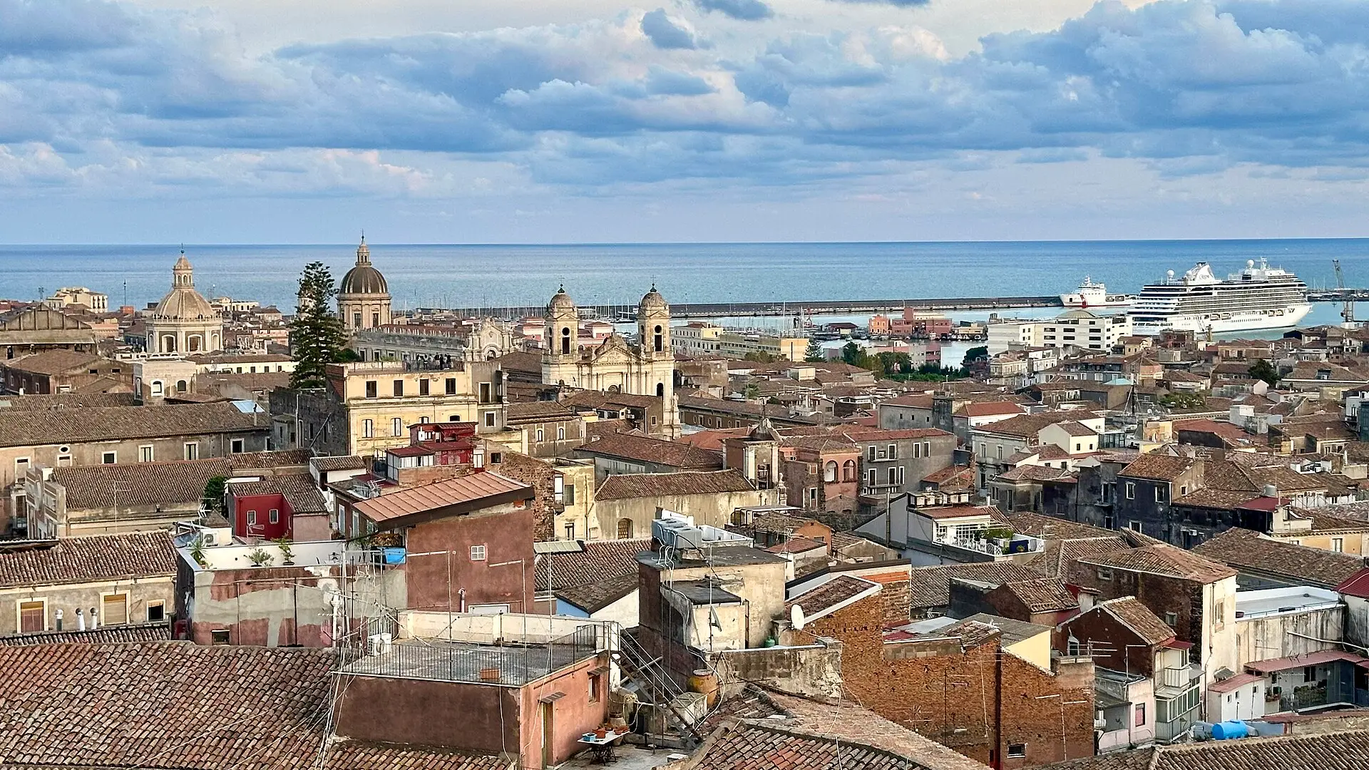 The rooftops and church domes of Catania seen from above, running down to the harbour and the sea