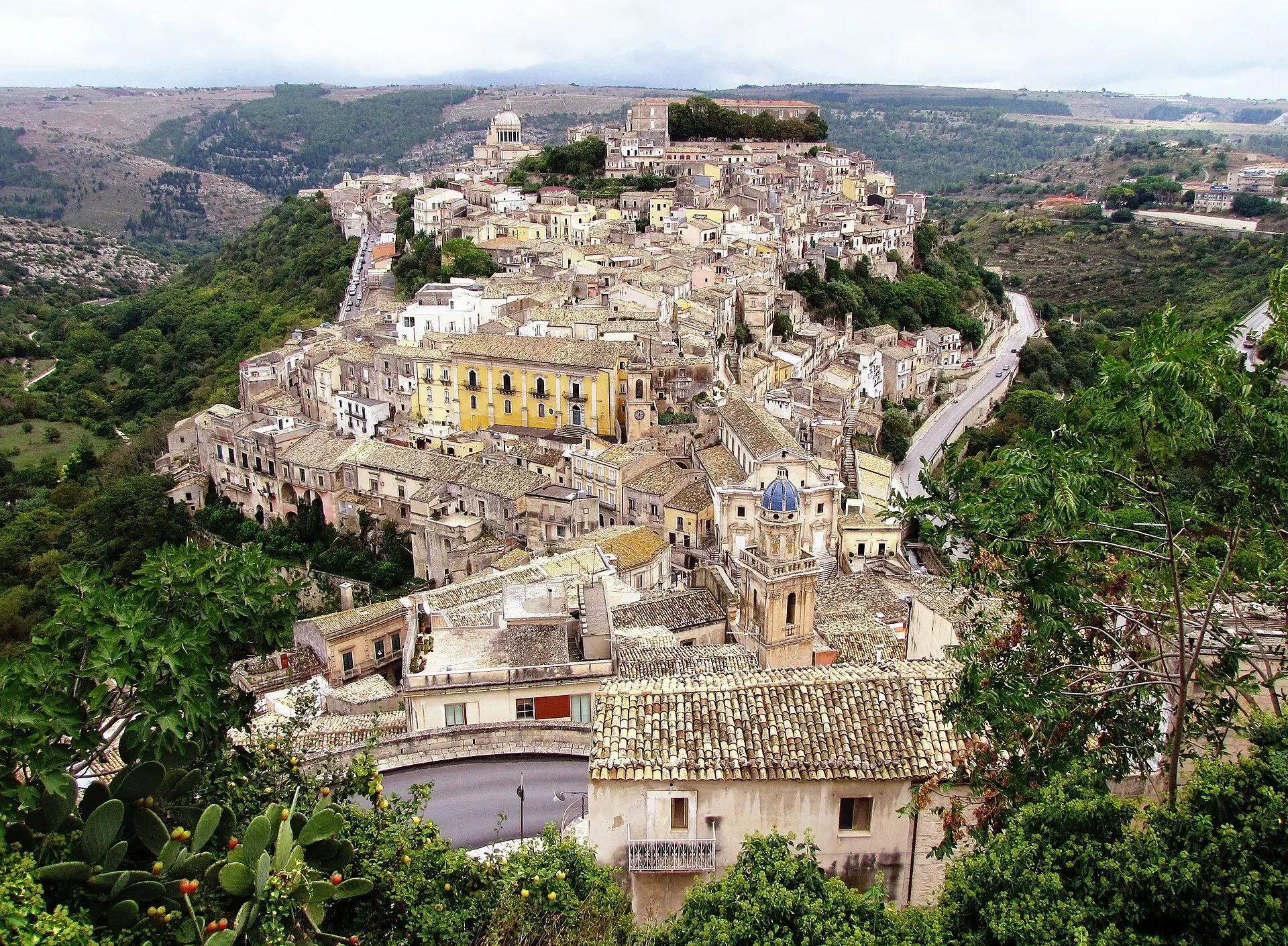 Ragusa Ibla seen from above, its stone houses and church domes packed along a ridge above a green valley